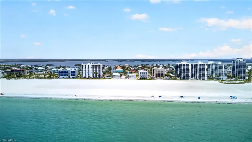 Expansive white sand beach with turquoise waters, featuring multiple beachfront high-rise buildings and distant coastal development