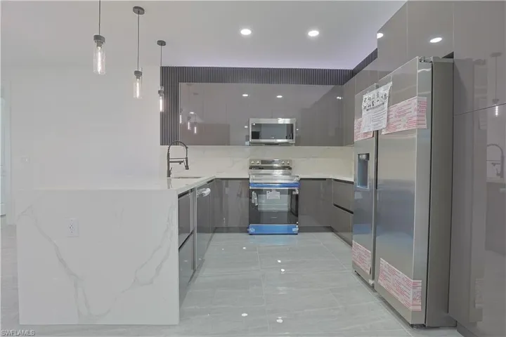 Kitchen with modern cabinets, light stone countertops, a peninsula, stainless steel appliances, and pendant lighting