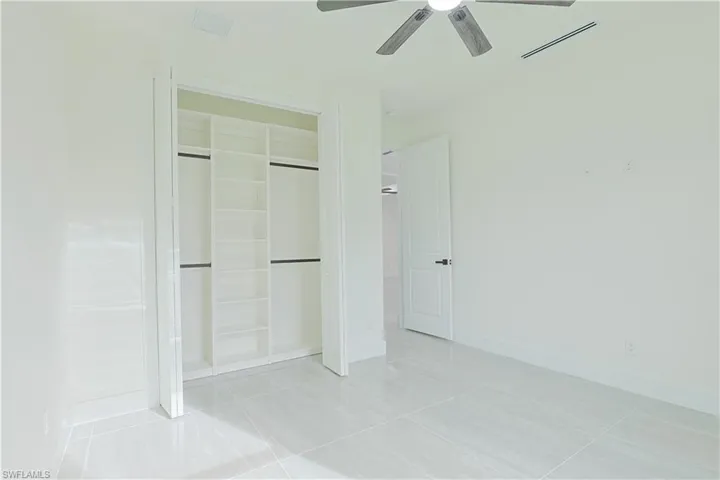 Bathroom with a walk in closet, light tile patterned floors, and ceiling fan