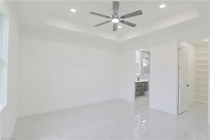 Unfurnished bedroom featuring a raised ceiling, a walk in closet, recessed lighting, light tile patterned floors, and ceiling fan
