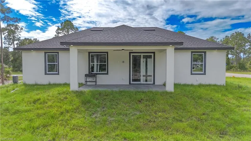 Back of house with a ceiling fan, a patio area, a lawn, and roof with shingles