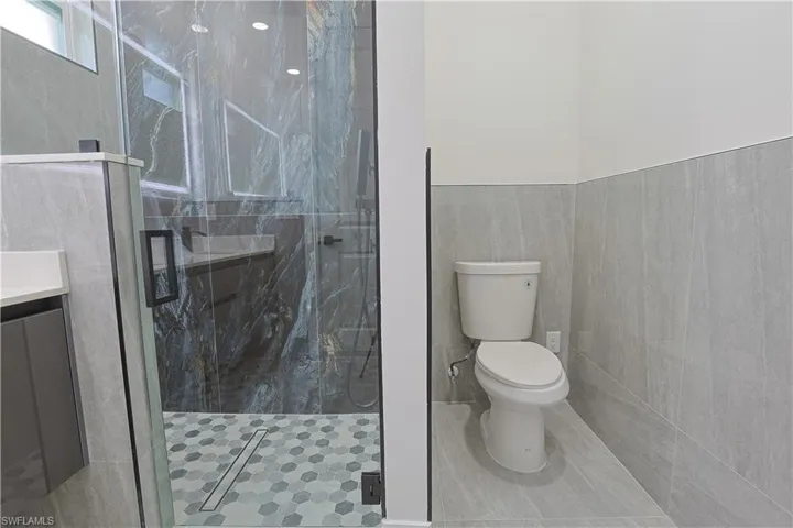 Full bathroom featuring tile walls, a marble finish shower, vanity, wainscoting, and tile patterned floors