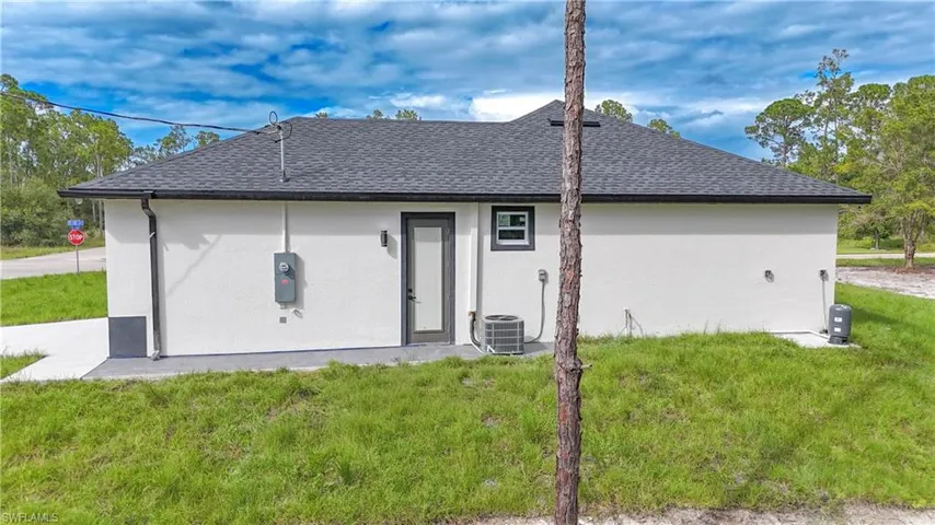 Back of property featuring a yard, stucco siding, and a shingled roof