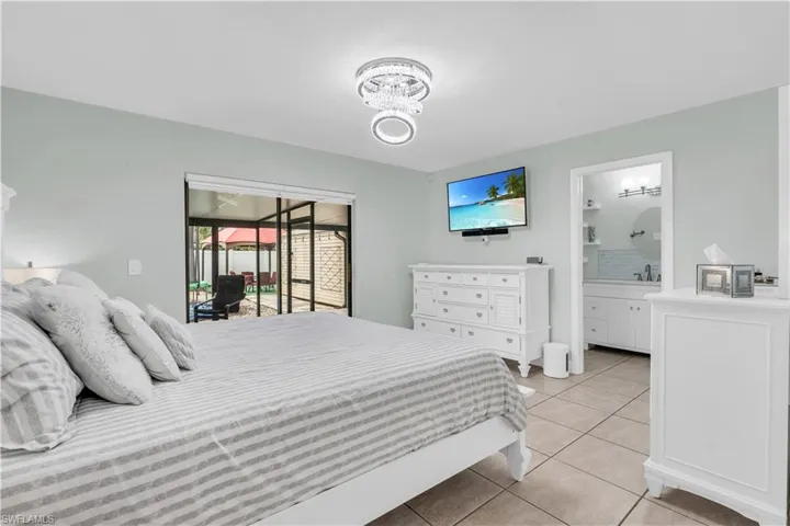 Tiled bedroom featuring ensuite bath, sink, a notable chandelier, and access to outside