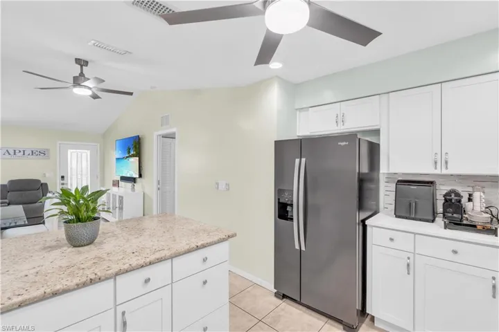 Kitchen featuring white cabinetry, decorative backsplash, light tile patterned floors, ceiling fan, and stainless steel refrigerator with ice dispenser
