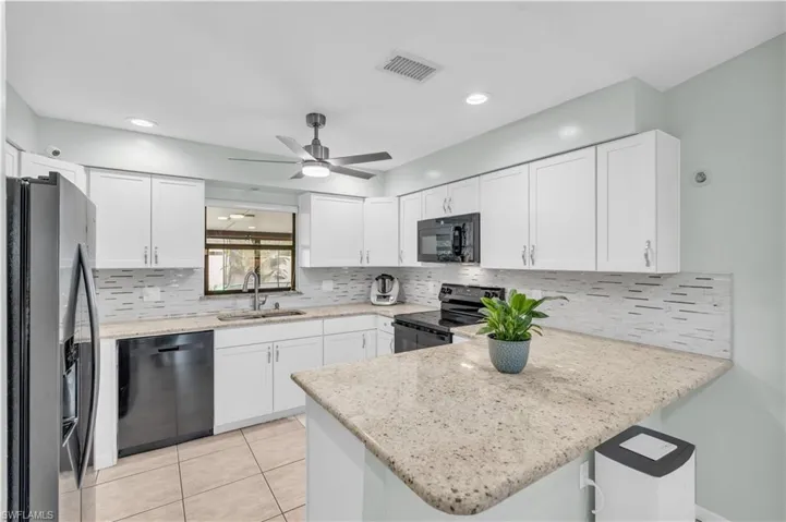 Kitchen with sink, black appliances, kitchen peninsula, and white cabinets