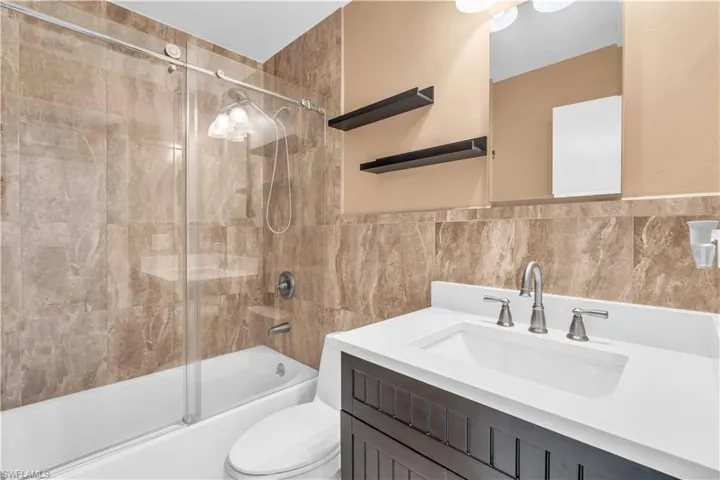 Full bathroom featuring bath / shower combo with glass door, tile walls, vanity, and toilet