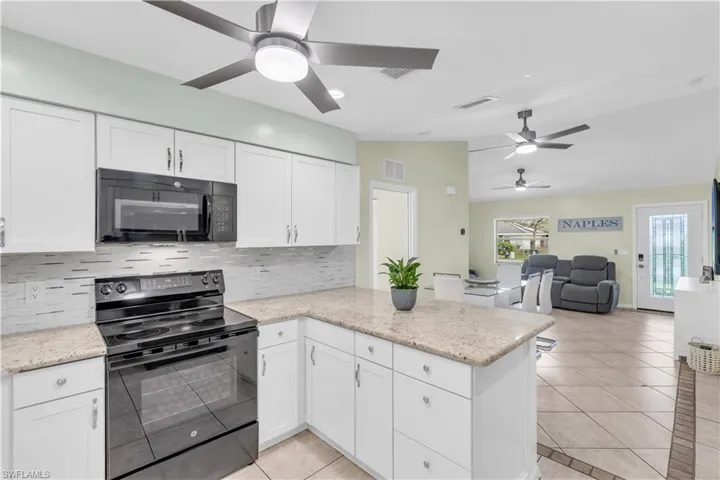 Kitchen with tasteful backsplash, white cabinets, kitchen peninsula, and black appliances