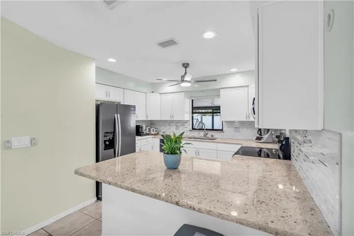 Kitchen with sink, white cabinetry, light stone counters, light tile patterned flooring, and kitchen peninsula