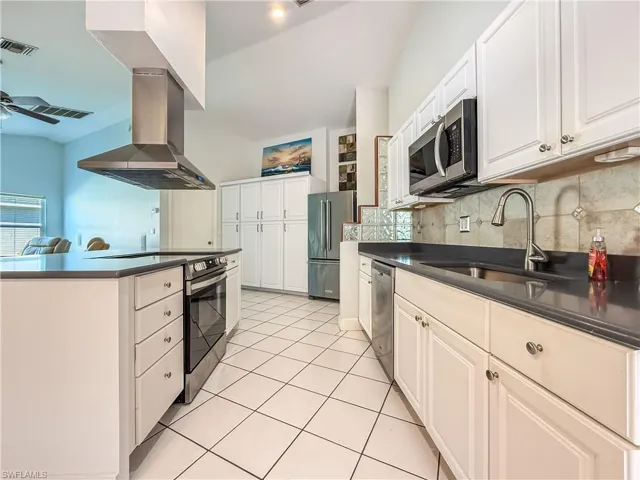 Kitchen featuring island range hood, stainless steel appliances, white cabinetry, and tasteful backsplash and  farm style sink