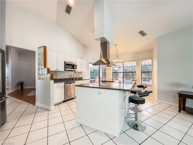 Kitchen featuring white cabinets, island range hood, a breakfast bar area, light tile patterned flooring, and appliances with stainless steel finishes