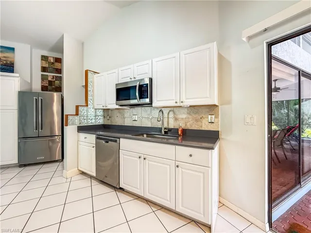 Kitchen featuring dark countertops, stainless steel appliances, white cabinets, light tile patterned floors, and high vaulted ceiling