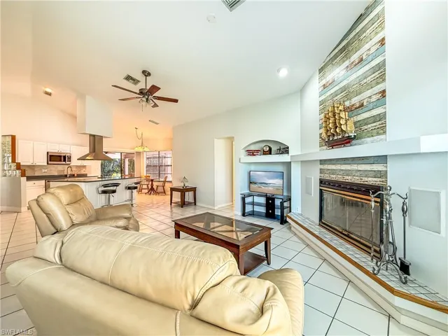 Great room featuring built in stone fireplace, light tile patterned floors, vaulted ceiling, and ceiling fan