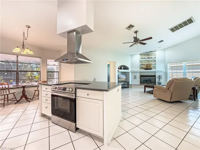 Kitchen featuring electric range, island range hood, open floor plan, white cabinetry, and a chandelier
