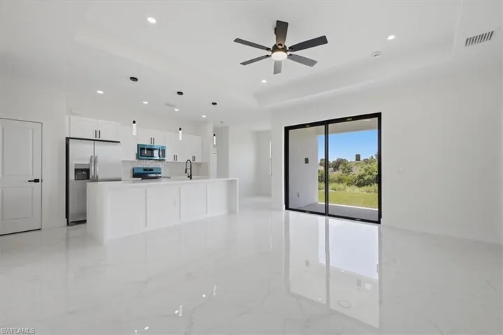 Contemporary kitchen featuring white cabinetry, stainless steel appliances, and a central island with a sink, complemented by polished tile flooring
