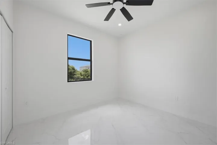 Bright room featuring a square window with dark framing, white walls, and white tile flooring