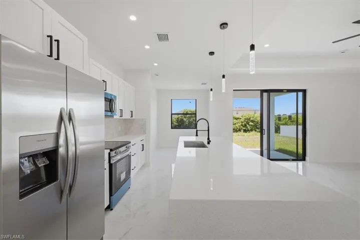 Modern kitchen featuring a large white quartz island with a black faucet, stainless steel appliances, white cabinetry with black hardware, and large format tile flooring