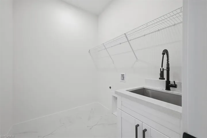 Utility room featuring a built-in sink with a matte black faucet, white cabinetry, and white countertop