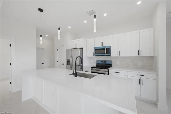 Modern kitchen featuring an expansive island with a built-in sink, white cabinetry, a light-toned tile backsplash, and stainless steel appliances