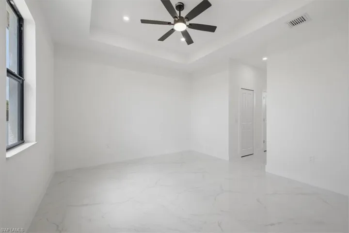 Spacious room featuring white tile flooring, tray ceiling, recessed lighting, and a ceiling fan with integrated light