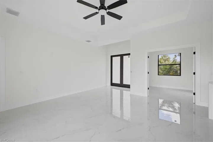 Spacious interior featuring large format tile flooring, a tray ceiling, and a modern ceiling fan