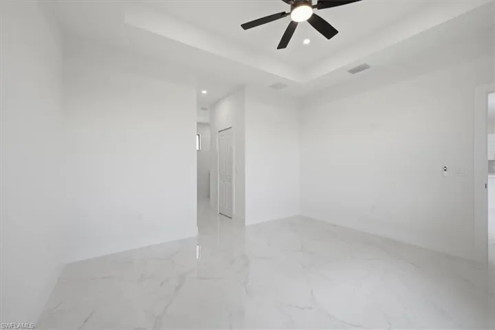 Spacious room featuring large format tile flooring, a tray ceiling with a ceiling fan, recessed lighting, and a paneled interior door