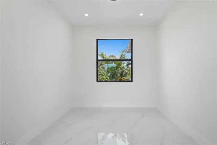 Bright interior space featuring a single window with black trim, white walls, white baseboards, and polished tile flooring