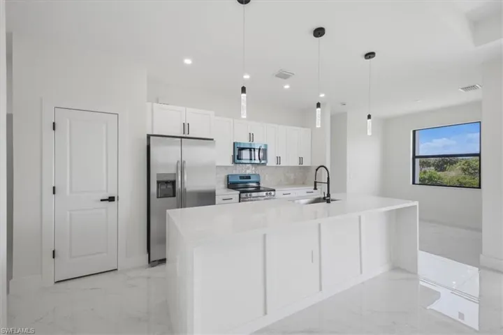 Modern kitchen featuring white cabinetry, stainless steel appliances, a center island with a sink and matte black faucet, pendant lighting, and large format tile flooring