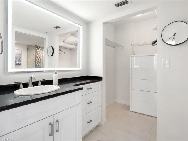 Bathroom vanity with a vessel sink, black countertop, and illuminated mirror