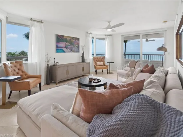 Open-concept living space featuring expansive windows and sliding glass doors, white ceiling fans, light-toned flooring, and a built-in console table