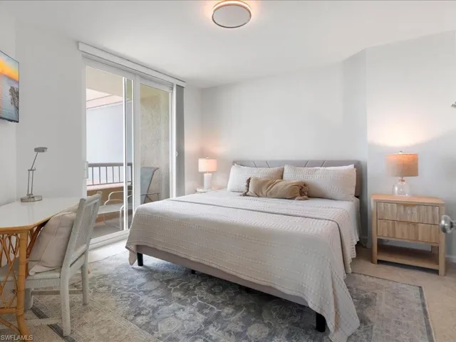 Bedroom featuring a private balcony with sliding glass doors, light gray upholstered bed frame, and wood-finish nightstand