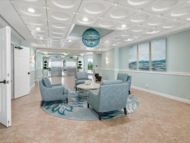 Lobby lounge featuring patterned ceiling tiles with recessed lighting, blue spherical chandelier, four armchairs surrounding a round coffee table, and large format floor tiling