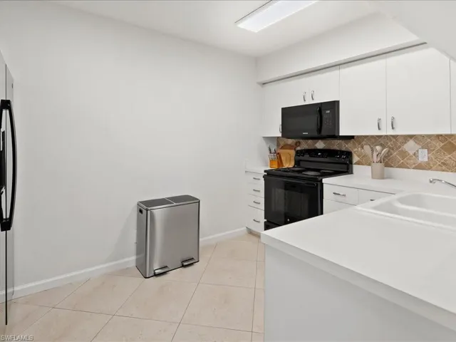 Contemporary kitchen featuring white cabinetry, a black appliance suite, light countertops, and a patterned tile backsplash