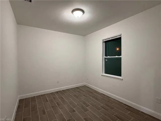 Empty room featuring baseboards and dark wood-style flooring