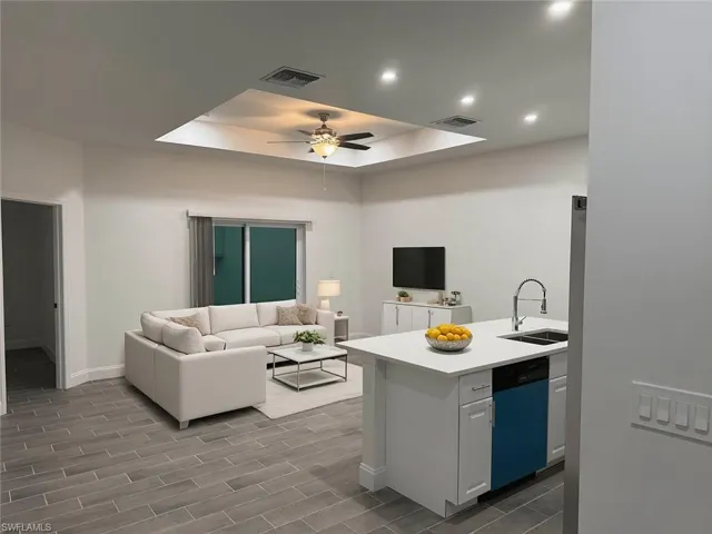 Kitchen featuring a tray ceiling, open floor plan, dishwashing machine, wood finish floors, and a peninsula