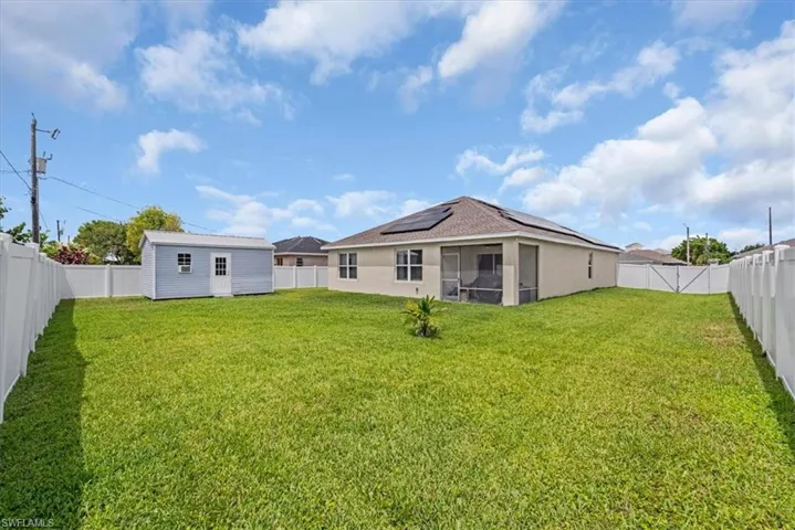 Expansive backyard featuring a manicured lawn, full white privacy fencing, and a detached storage shed
