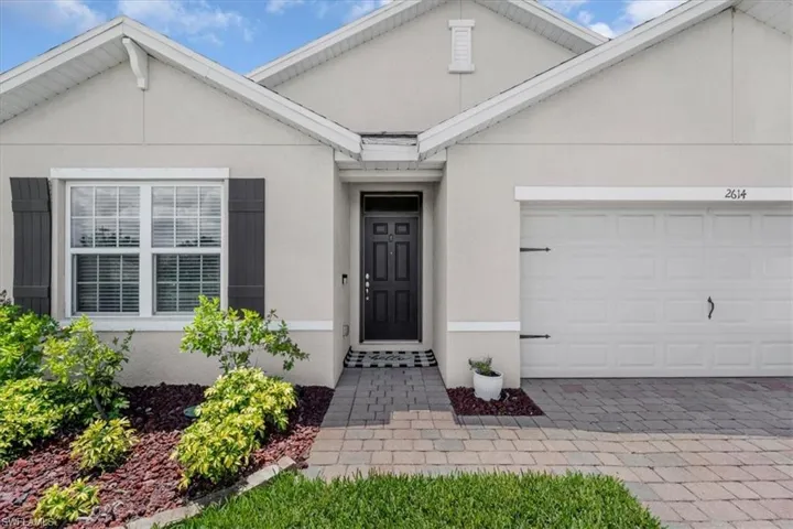 Stucco exterior with a dark paneled entry door, complemented by a paver walkway and mature landscaping