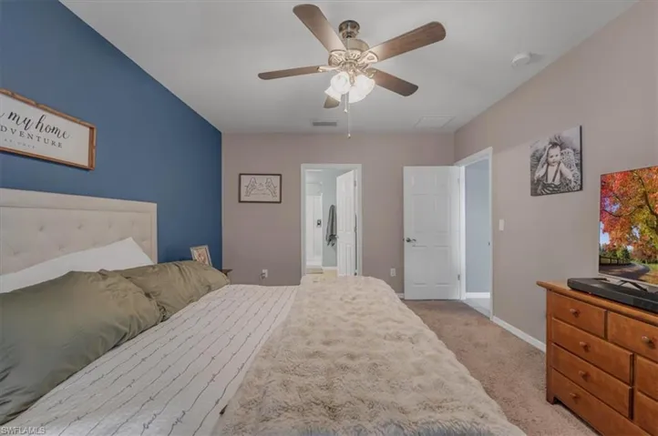 Spacious bedroom featuring an accent wall, ceiling fan with integrated lighting, paneled interior doors, and neutral carpeting