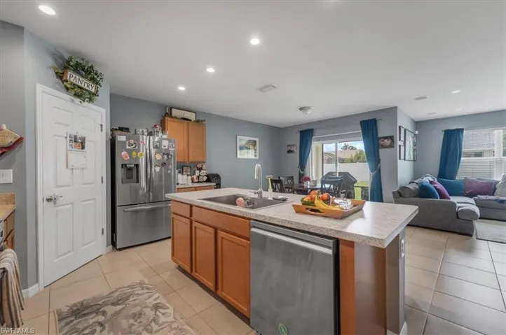 Kitchen featuring a central island with an integrated sink, stainless steel appliances, recessed lighting, and wood-finish cabinetry