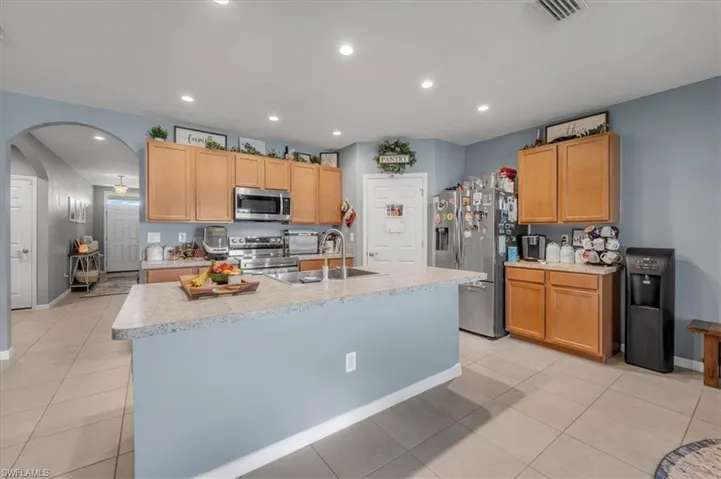 Kitchen featuring an island with a built-in sink, light wood-finish cabinetry, stainless steel appliances, recessed lighting, and tile flooring