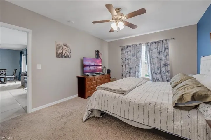 Carpeted bedroom with a ceiling fan, a window with blinds, and an adjacent doorway leading to a tiled area