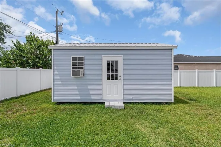 Detached structure with light blue siding, a white entry door, and a window with an integrated air conditioning unit