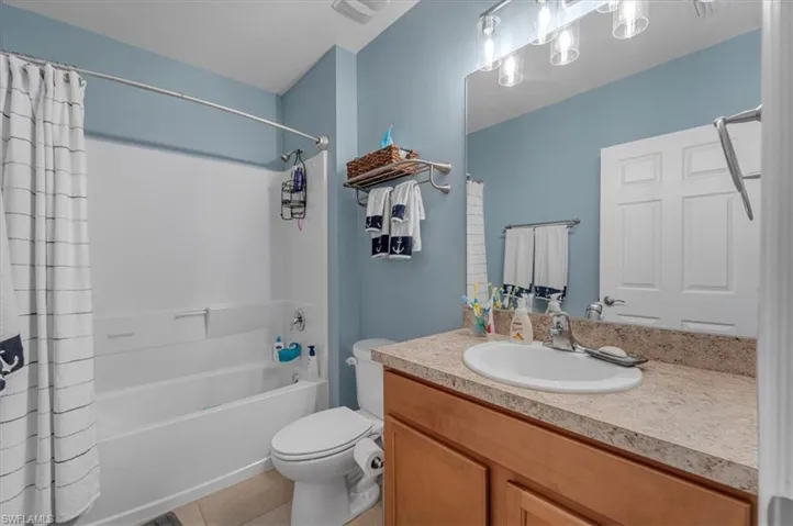 Bathroom featuring a full-sized bathtub with shower, a vanity with an integrated sink, a light-toned countertop, and wood-finish cabinetry