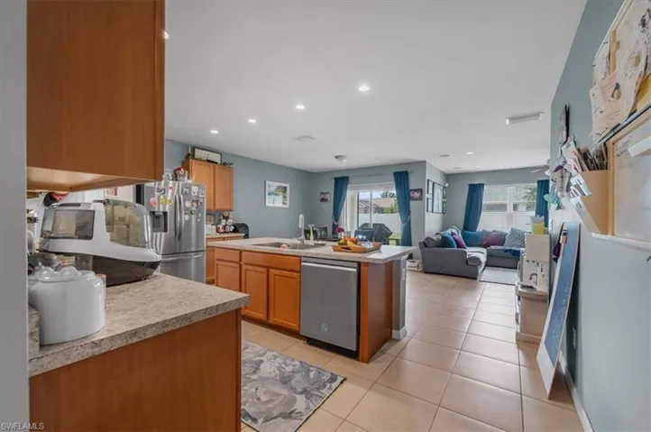 Open-concept living space with a kitchen island, recessed lighting, tile flooring, stainless steel appliances, and wood-finish cabinetry