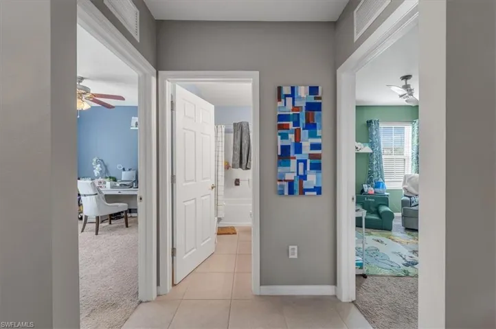 Hallway with light gray walls and tile flooring, featuring three doorways leading to distinct interior spaces