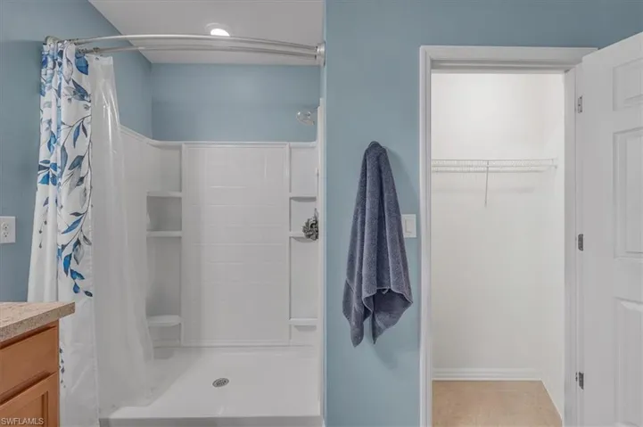 Bathroom featuring a shower with built-in shelving, a curved shower rod, and a light wood-finish vanity with a stone-finish countertop