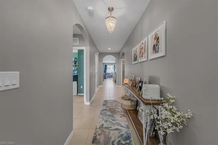 Hallway featuring tile flooring, arched doorways, a decorative chandelier, and light gray wall paint