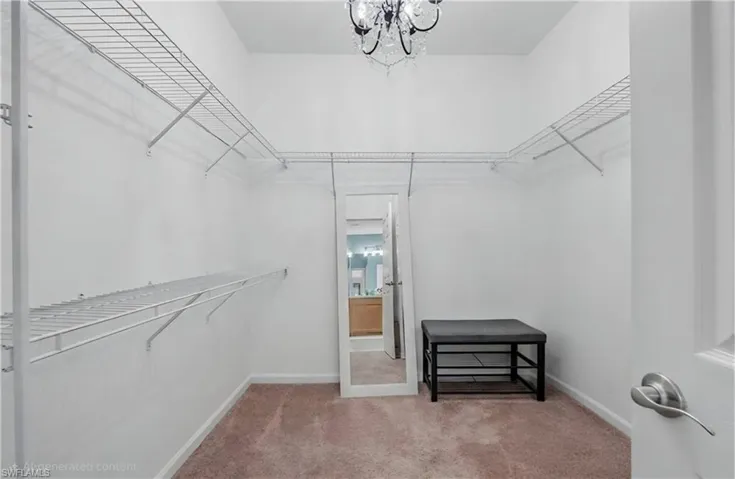 Walk-in closet featuring built-in wire shelving, plush carpet flooring, a decorative chandelier, and white wall finishes