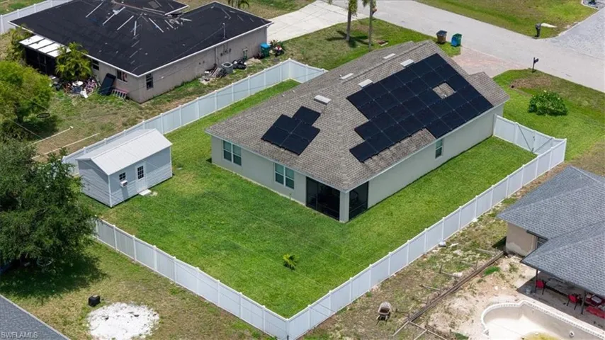 Rear exterior featuring a full white vinyl fence, spacious green lawn, and a separate storage shed with a metal roof