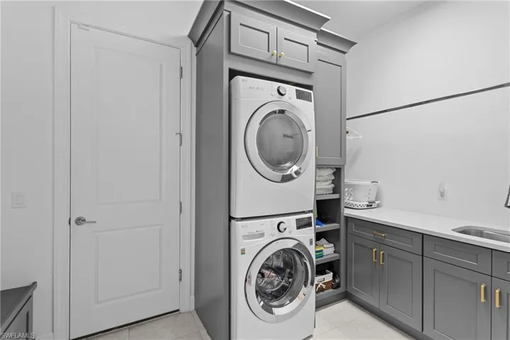 Laundry room with stacked washer and clothes dryer, cabinet space, a sink, and light tile patterned flooring